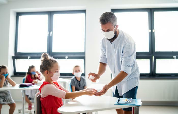 COVID-19 classroom with teacher sanitizing children's hands