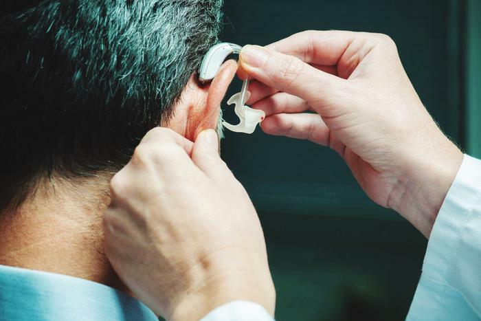 Doctor putting hearing aid on man