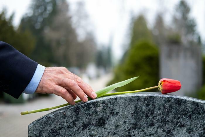 Grieving person placing flower on tombstone