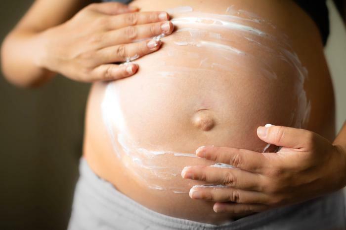 Pregnant woman using lotion on belly