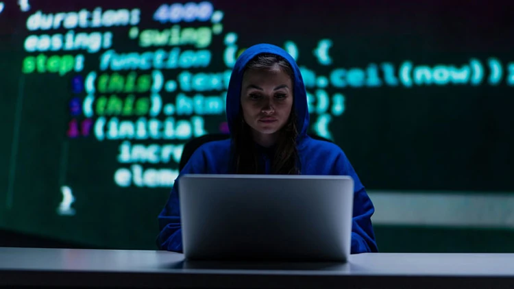 Scammer sitting in front of a laptop with a line of code behind her