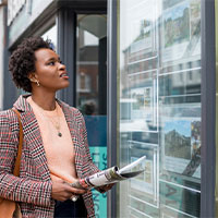 woman looking at various property for sale ads in a shop window