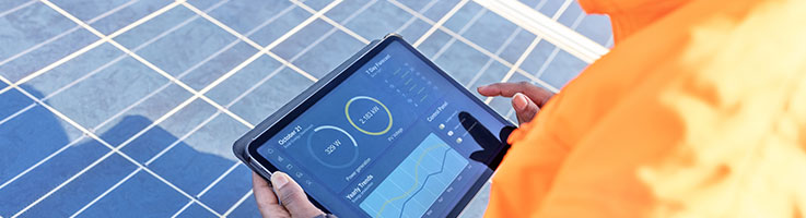 over the shoulder view of a field technician holding a digital tablet showing a solar power panel monitoring app