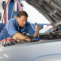 mechanic inspecting under the hood of car