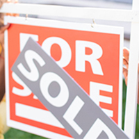 man putting sold sign on a for sale sign in front of house