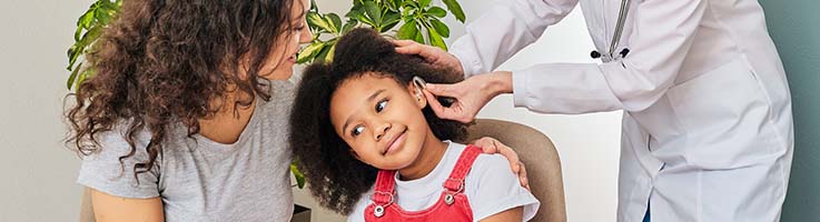 audiologist inserting hearing aid into childs ear