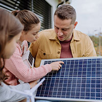 father and daughters holding a solar panel