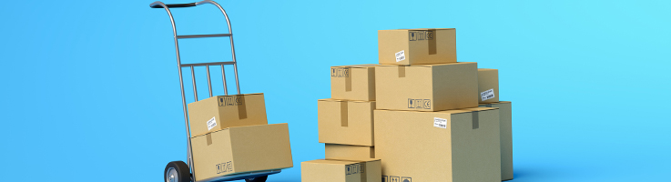 two cardboard boxes on hand truck beside a stack of other cardboard boxes