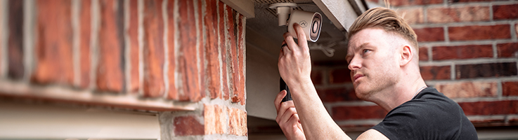 man attaching an outdoor security camera to his house