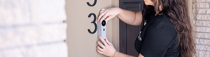 woman installing doorbell camera on her house