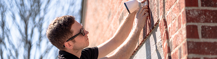 man installing security camera on the side of a house