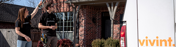 woman standing in front of home with home security technician