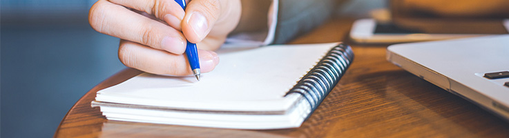 woman filling out notebook next to a laptop