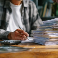a man writing on a desk with a stack of papers on it