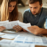 a couple looking at different bills on a kitchen table