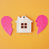 wooden miniature house with half of a broken heart on the left and right sides and bright orange in the background