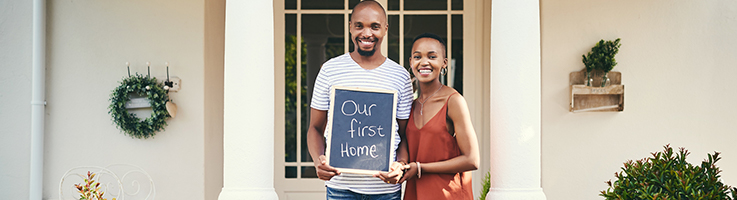 couple holding a sign outside their first home