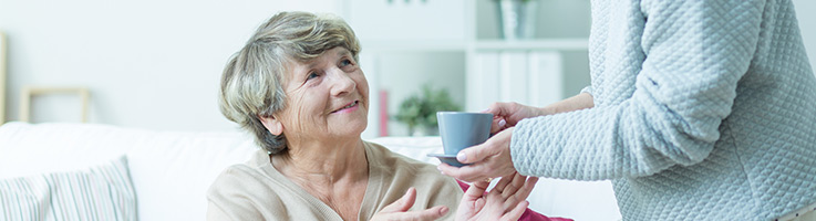 daughter handing her older mother a cup of coffee