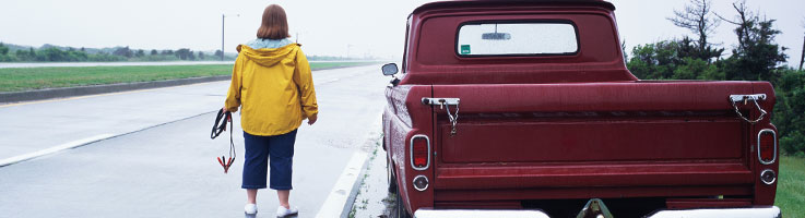 rear view of a woman standing near a truck while holding jumper cables