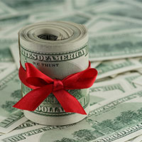roll of dollars tied with red ribbon placed on top of more dollars