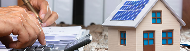 man doing calculations beside by a miniature home with solar panels