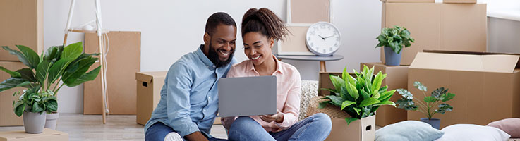 couple in front of moving boxes looking at laptop screen