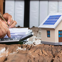 man doing calculations beside by a miniature home with solar panels