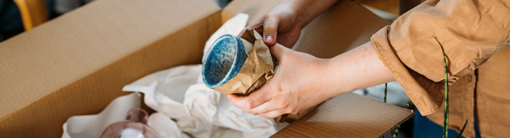 woman wrapping and packing a mug in moving box