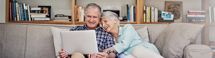 older couple sitting on a couch looking at a laptop