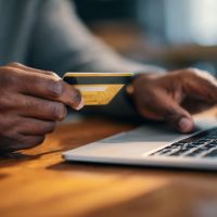 a man seated at his laptop with a credit card in hand