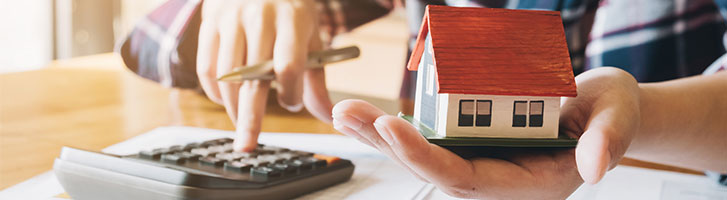 woman using the calculator and holding miniature house