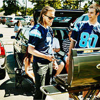 smiling friends wearing team jersey barbecuing in a stadium parking lot
