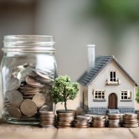 miniature house and trees beside a jar of coins
