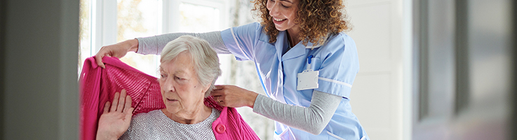 nurse helping put sweater on elderly woman