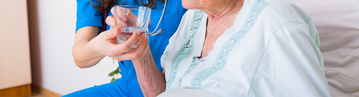 older woman taking a drink of water with the help of a nurse