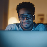 a male young adult smiling while looking at a computer monitor