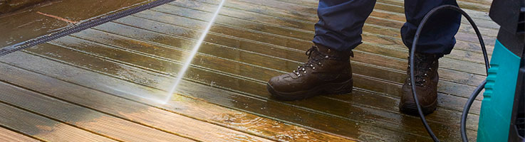 man with pressure washer cleaning a wooden deck