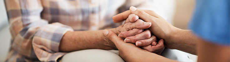 nurse holding an old woman's hands in comfort