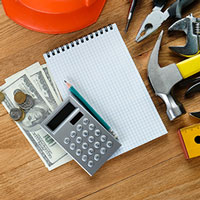 calculator and cash, notepad and pencil, and partial shot of hand tools and ruler placed on a wooden table