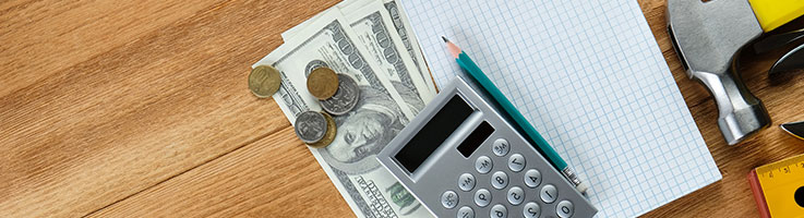 calculator and cash, notepad and pencil, and partial shot of hand tools and ruler placed on a wooden table