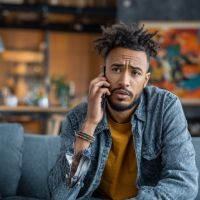 a man answering his cellular phone while sitting on a sofa