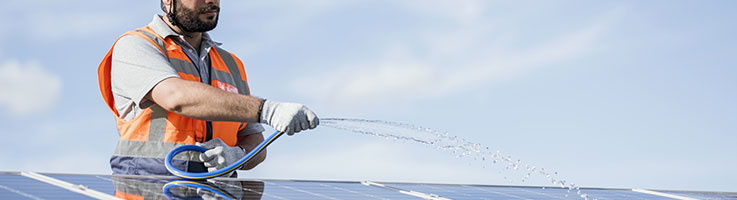 technician using a hose to spray solar panels with water
