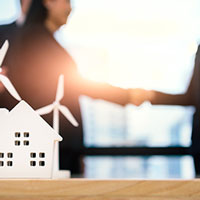 closeup of house and windmill props with business people doing handshake on the background