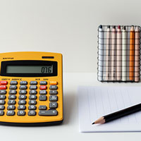 a yellow calculator beside a pencil on a notepad and a set of dermatograph pencils in different colors.